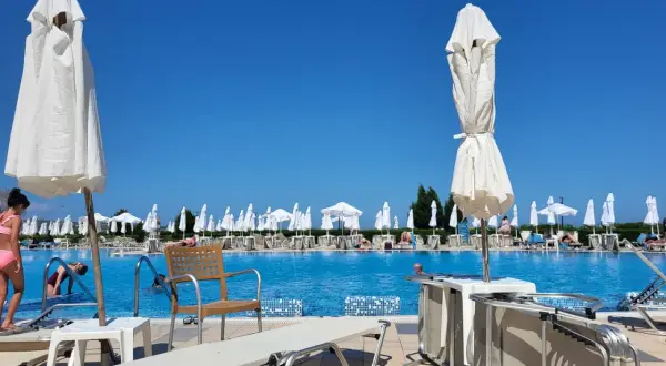 Basen hotelowy z leżakami i parasolami pod błękitnym niebem.